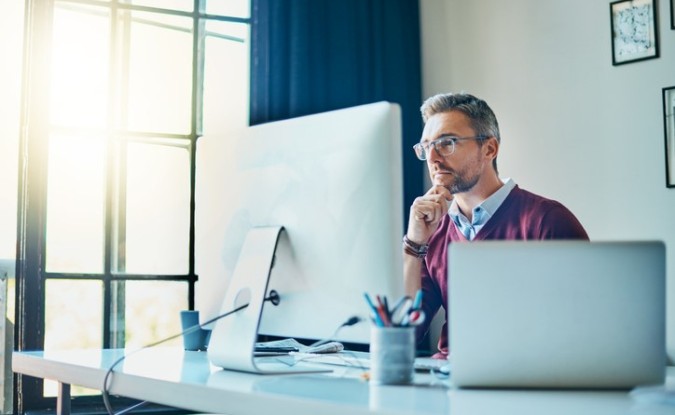 Man looks thoughtfully at his computer screen, resting his chin on his hand.