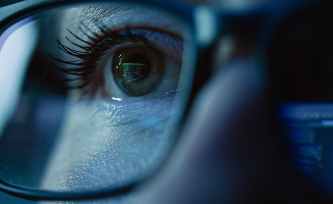 Close up on person working at a computer. The monitor is reflected in their glasses.