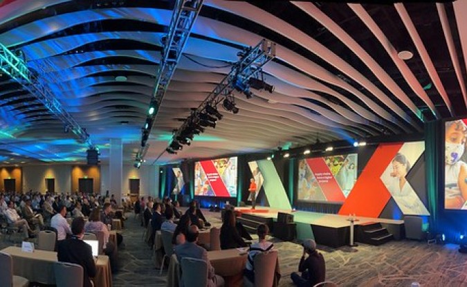 A wideangle view of the Kinexions '22 audience in a large conference hall, watching a speaker on mainstage.