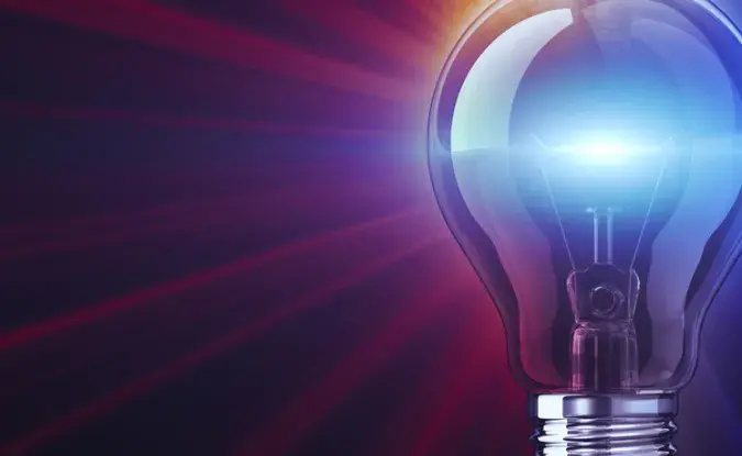 A lightbulb radiates bright blue and purple light against a dark background.