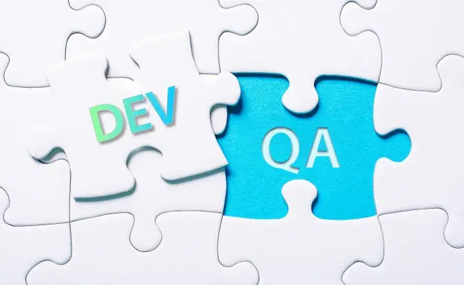 White puzzle pieces. One overlaid puzzle piece has the word "DEV" in green and blue letters. The letters "QA" appear in a blue space on the puzzle board.