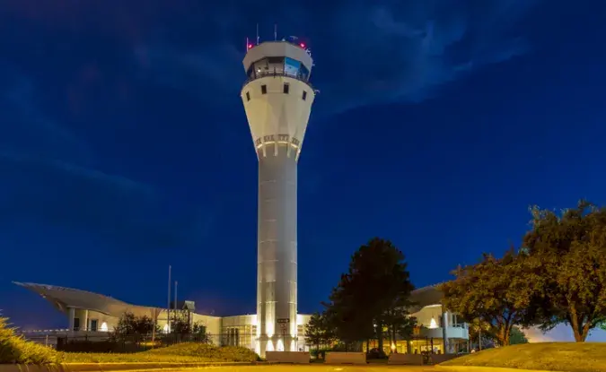 A control tower at an airport is lit up against the night sky.