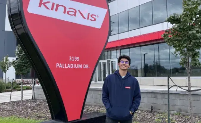 Kinaxis employee Tejas Khare stands outside the office next to the Kinaxis logo signage.