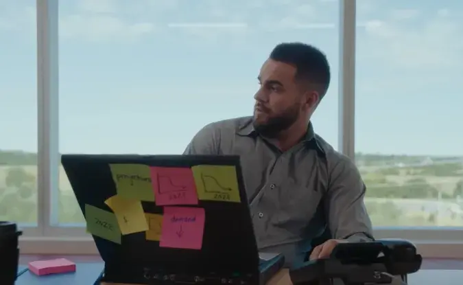 Supply chain planner sits at a desk with a laptop covered in sticky notes that indicate demand and supply trends.