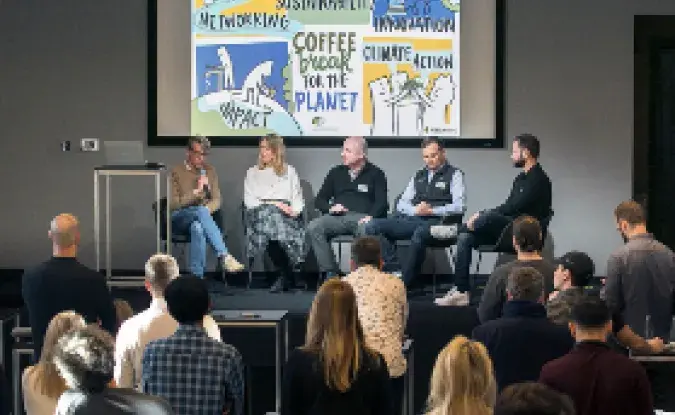 An audience of several people faces five people on a stage for a Coffee for the Planet live event. 