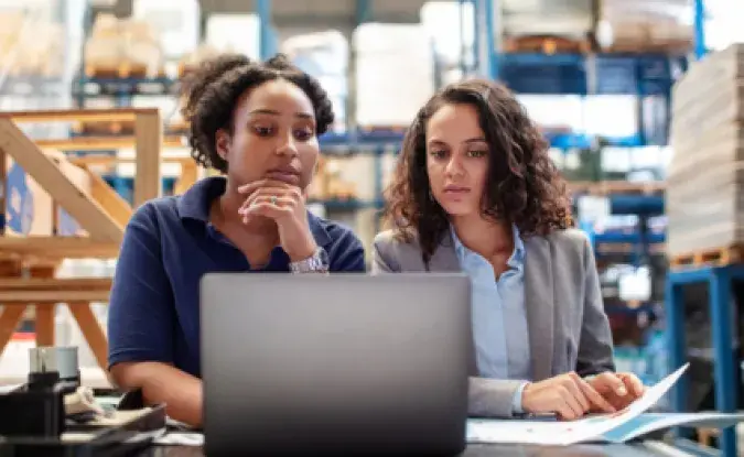 Two women in a warehouse looking at a laptop