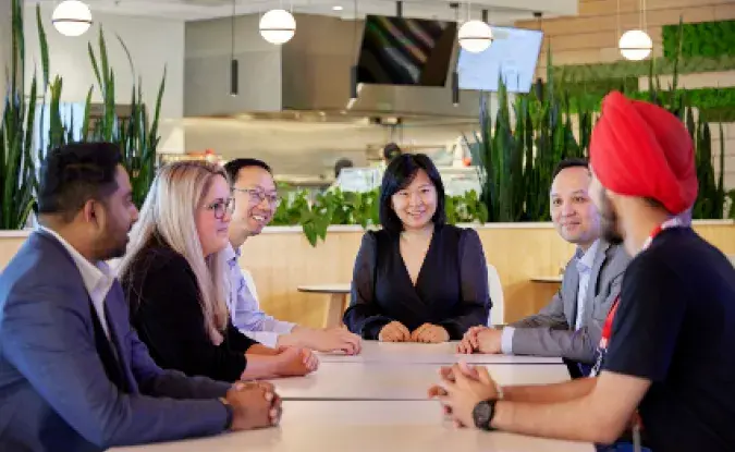 Diverse group of Kinaxis employees talks at a table in Kinaxis headquarters office 