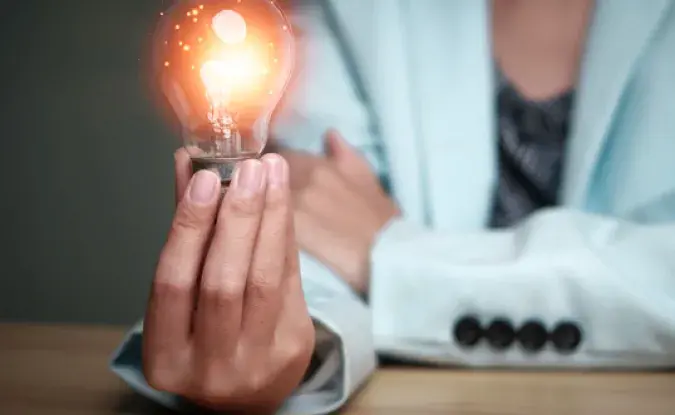 Businesswoman holding a light bulb filled with sparks, representing a creative new idea. Innovation, brainstorming, solution and inspiration concept.    