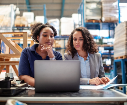 Two women in warehouse looking at a laptop screen